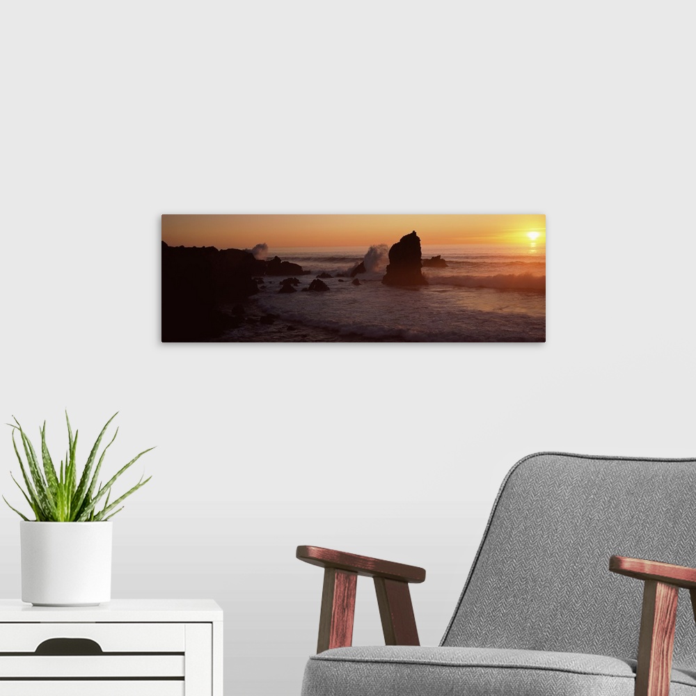 A modern room featuring Panoramic photo on canvas of rock formations on a beach with waves breaking on the shore at sunset.