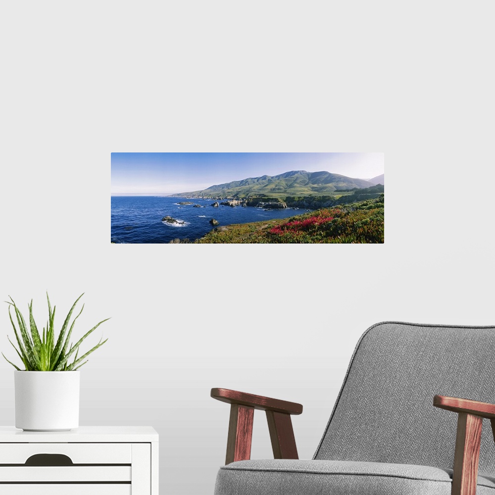 A modern room featuring Horizontal, oversized photograph of blue waters with protruding rocks, mountains in the distance,...
