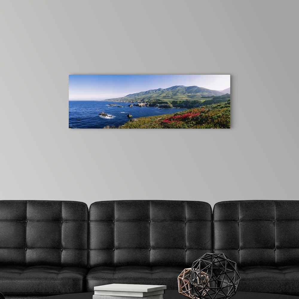 A modern room featuring Horizontal, oversized photograph of blue waters with protruding rocks, mountains in the distance,...