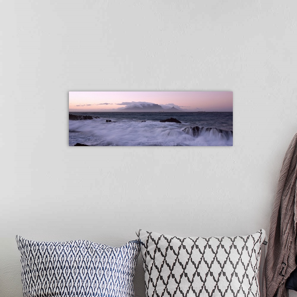 A bohemian room featuring Waves from the rising tide crash over the rocky coastline at twilight. In the distance clouds for...