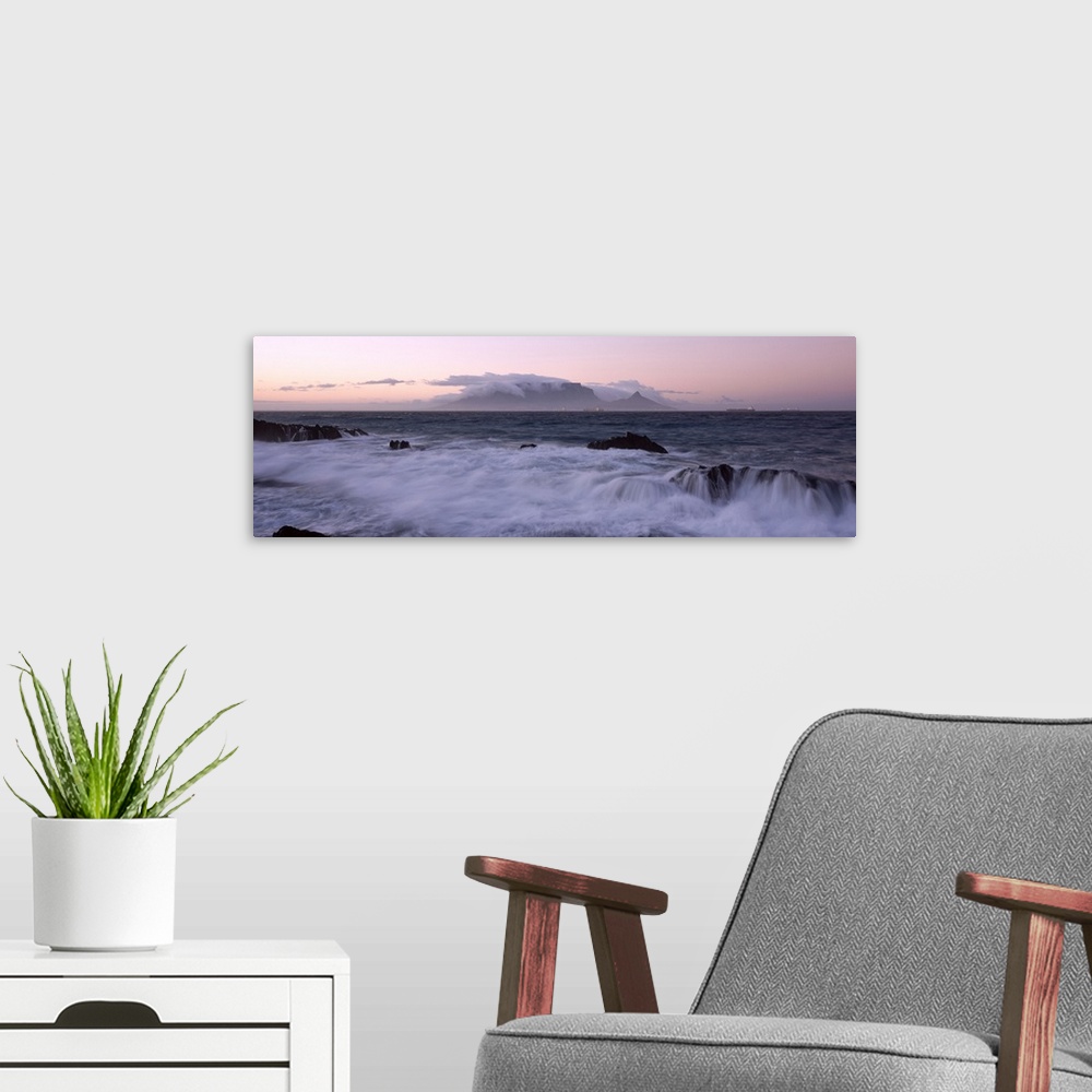 A modern room featuring Waves from the rising tide crash over the rocky coastline at twilight. In the distance clouds for...