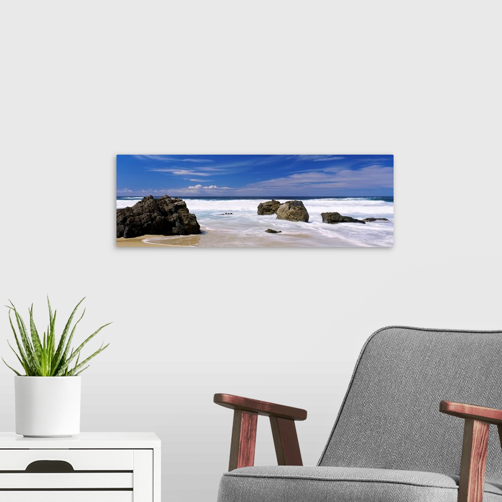 A modern room featuring Panoramic photograph of large boulders sitting on a beach in Big Sur, California (CA) on a sunny ...