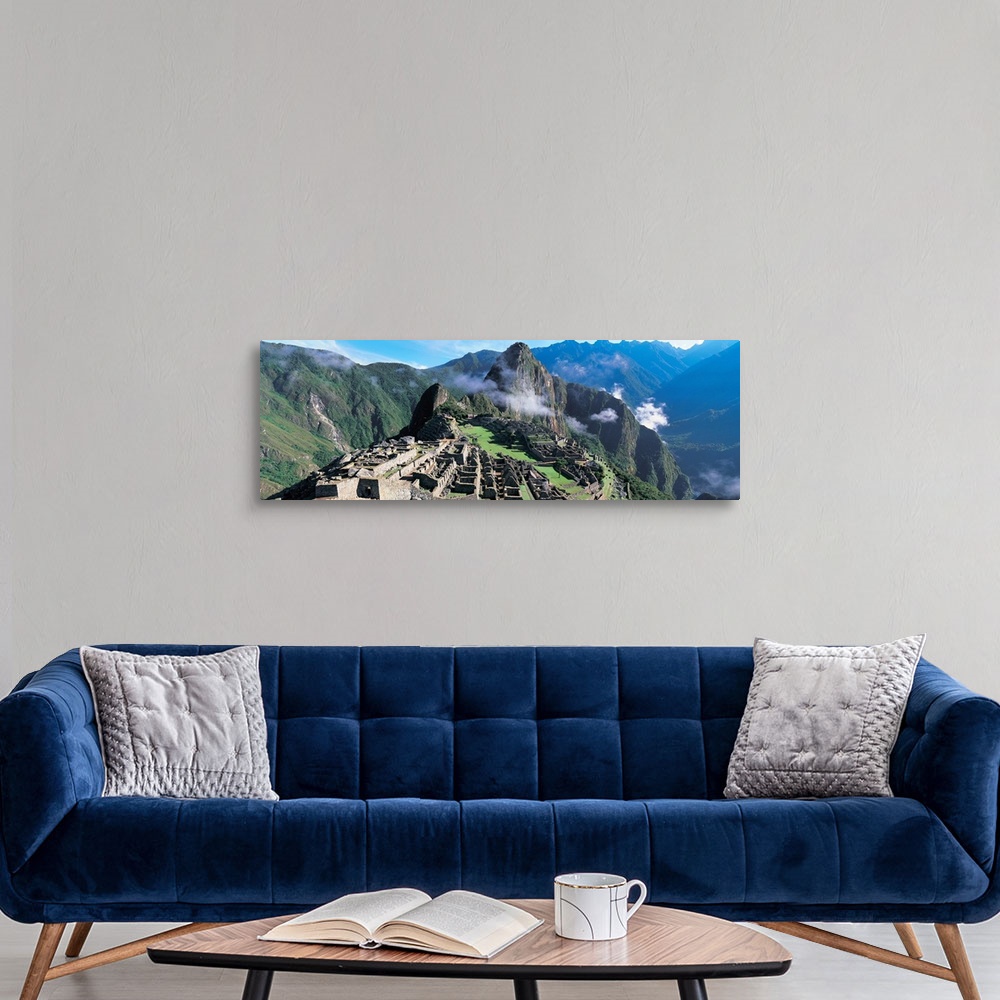 A modern room featuring Ruins of an ancient civilization lay on a hill under a towering mountain in a valley in South Ame...
