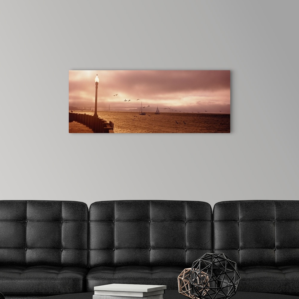 A modern room featuring Dense fog covers most of the Golden Gate Bridge in the distance while two sail boats cruise in th...