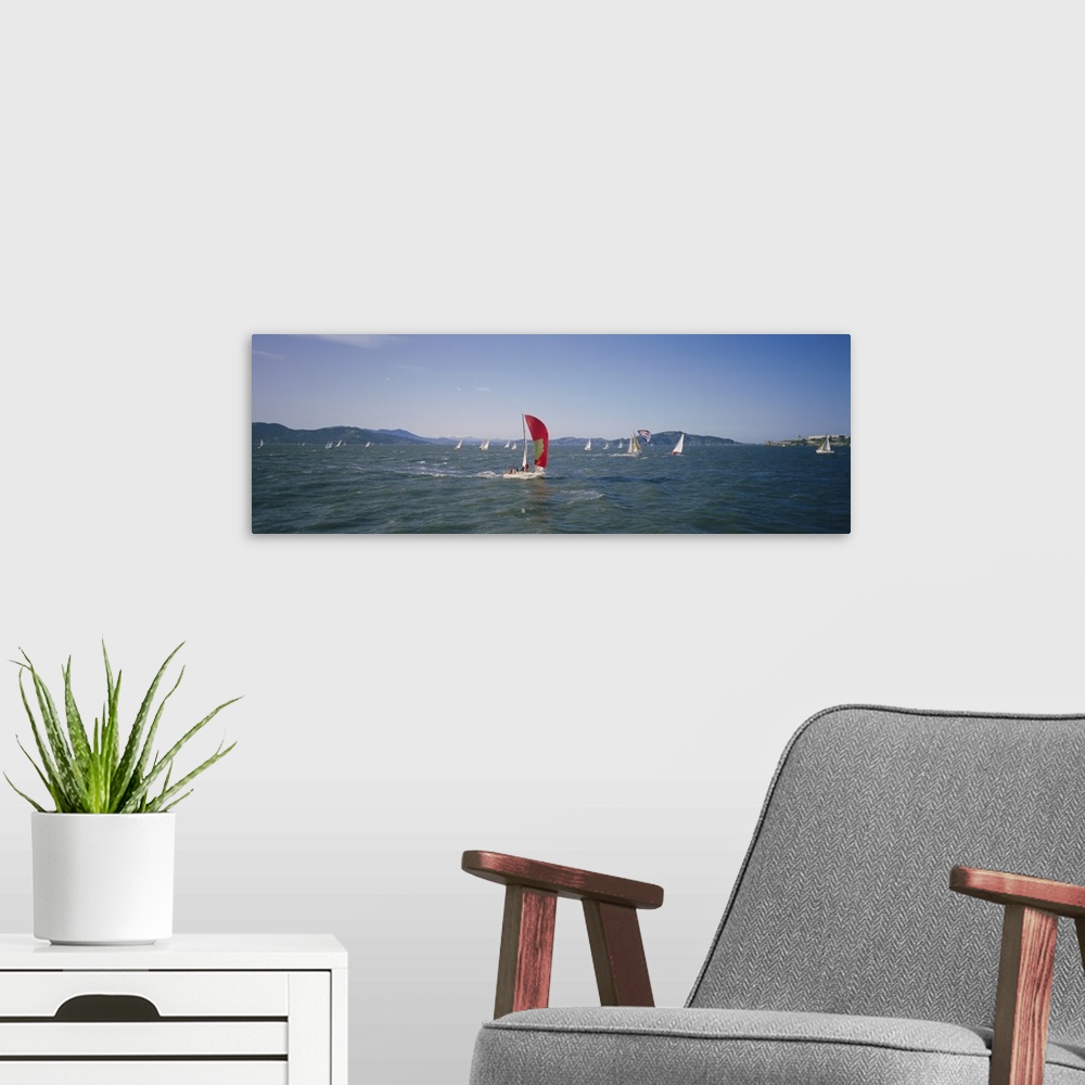 A modern room featuring Panoramic photograph ocean with scattered boats with sails and mountains in the distance under a ...