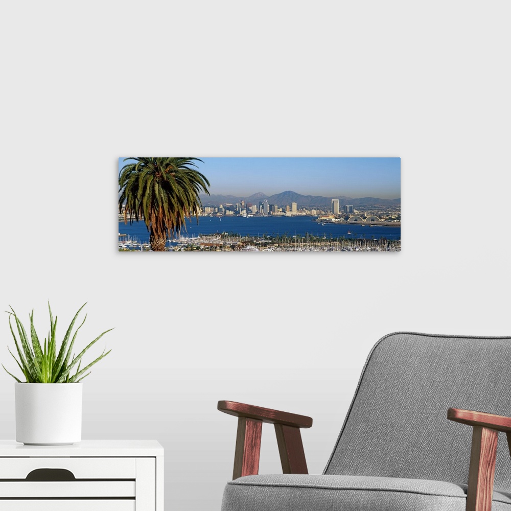 A modern room featuring A large panoramic view of the San Diego skyline with water shown in front and sail boats standing...
