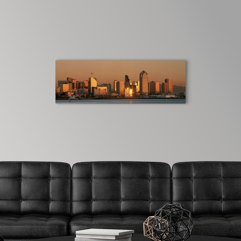 A modern room featuring This wall art is a panoramic photograph of the city skyline reflecting the fading sunlight.