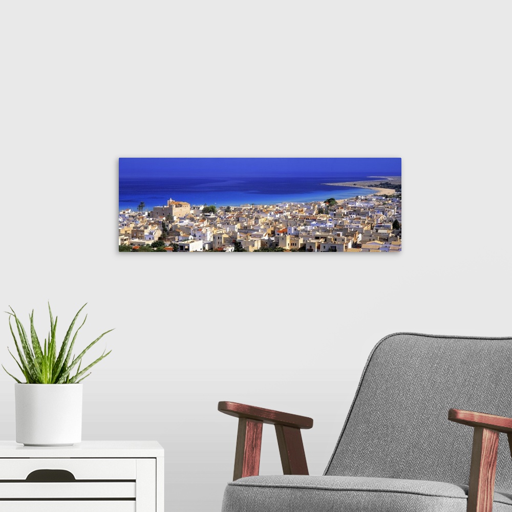 A modern room featuring This is a landscape photograph of a coastal village and the sea beyond it in this panoramic wall ...