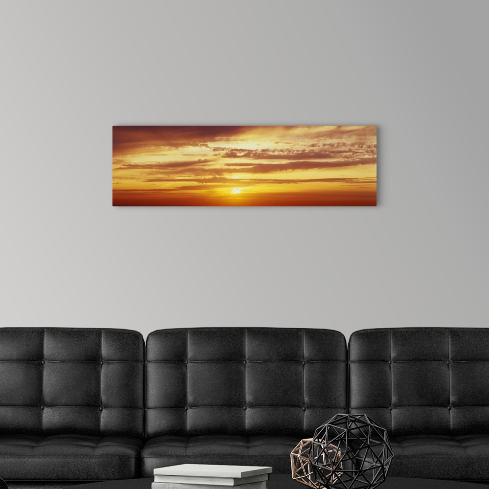 A modern room featuring Panoramic photo on canvas of a brightly colored sunset with horizontal clouds.
