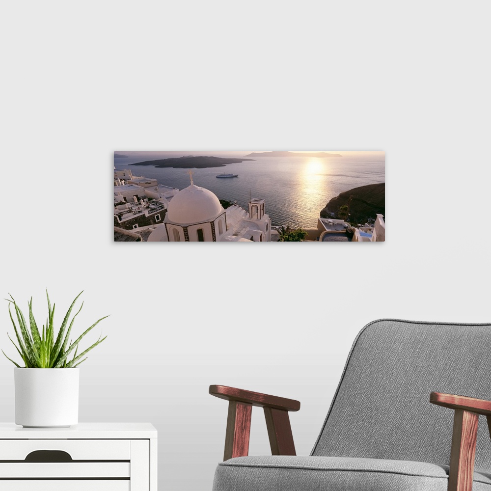A modern room featuring Giant, high angle photograph of the tops of buildings, looking out onto the water in Santorini, G...