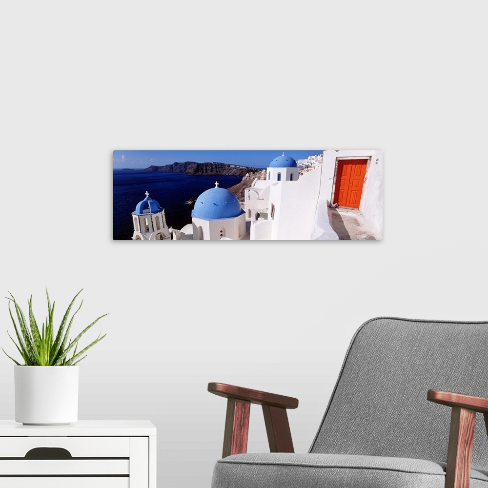 A modern room featuring Panoramic photograph of whitewashed buildings with colorful roofs near coastline with mountains i...