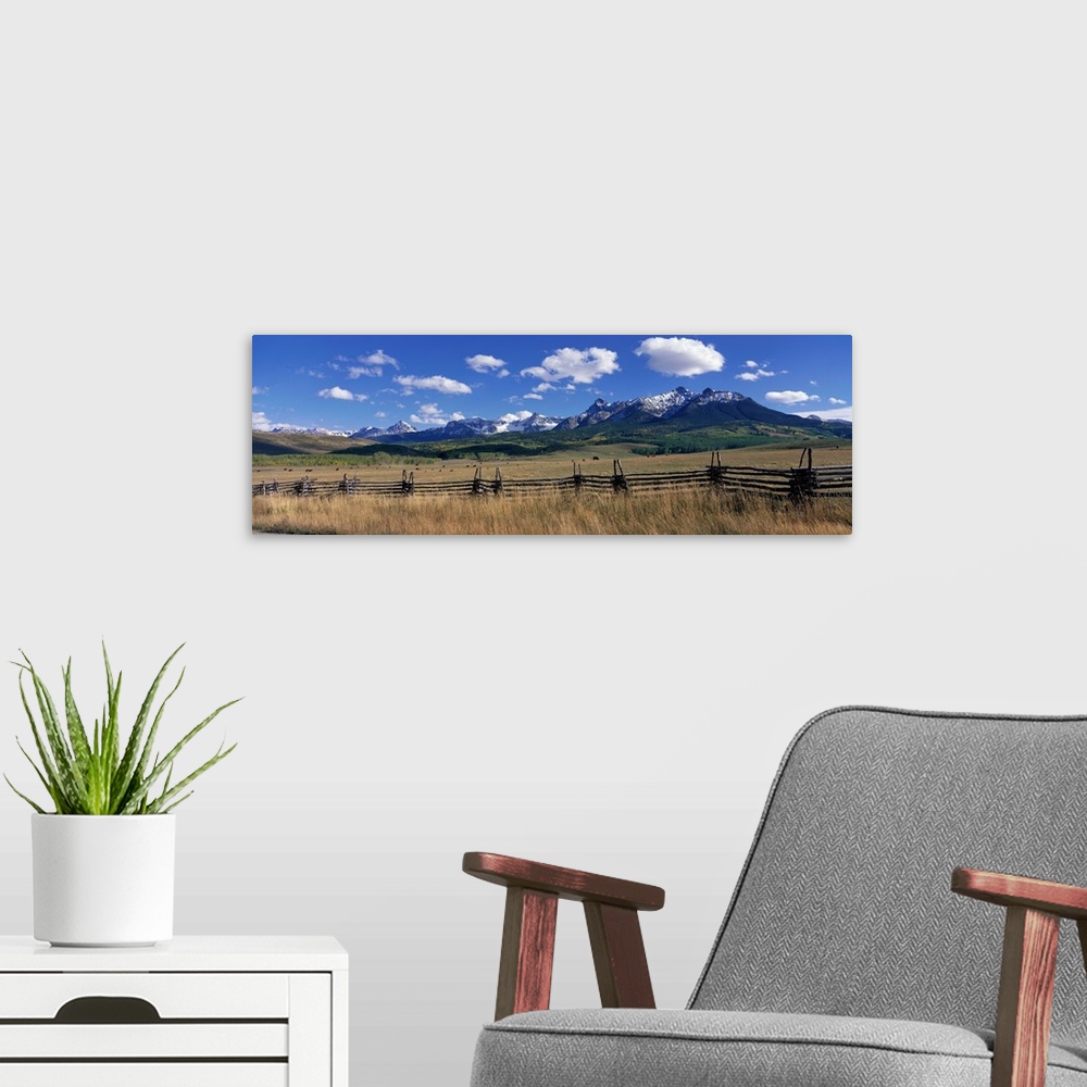 A modern room featuring Horizontal, large photograph of a distant mountain range beneath a bright blue sky, cattle grazin...