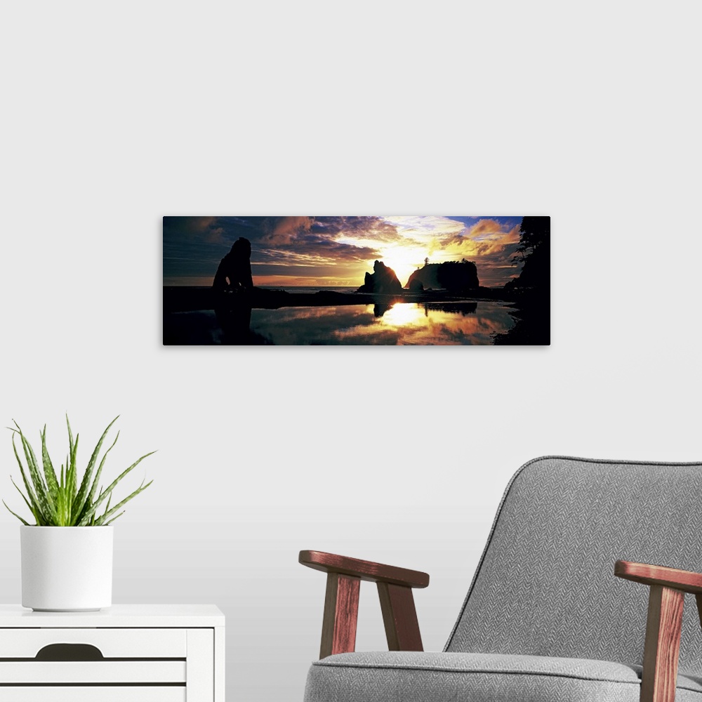 A modern room featuring Panoramic photograph of huge rock formations in the ocean under a dark cloudy sky at sunset.
