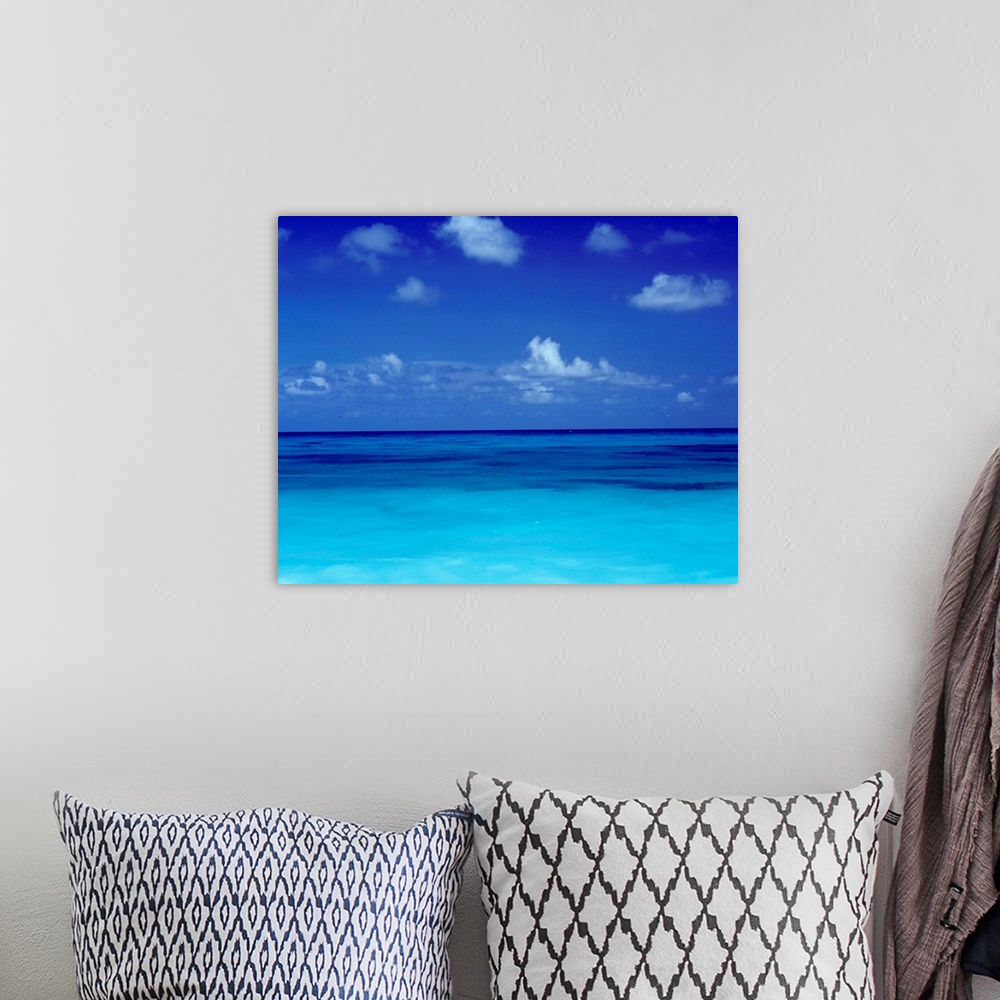 A bohemian room featuring Big square photo art of a clear ocean with puffy clouds in a blue sky.