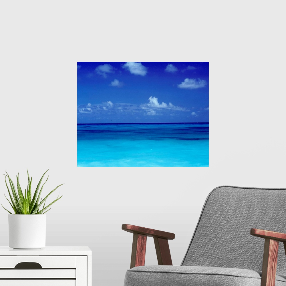 A modern room featuring Big square photo art of a clear ocean with puffy clouds in a blue sky.