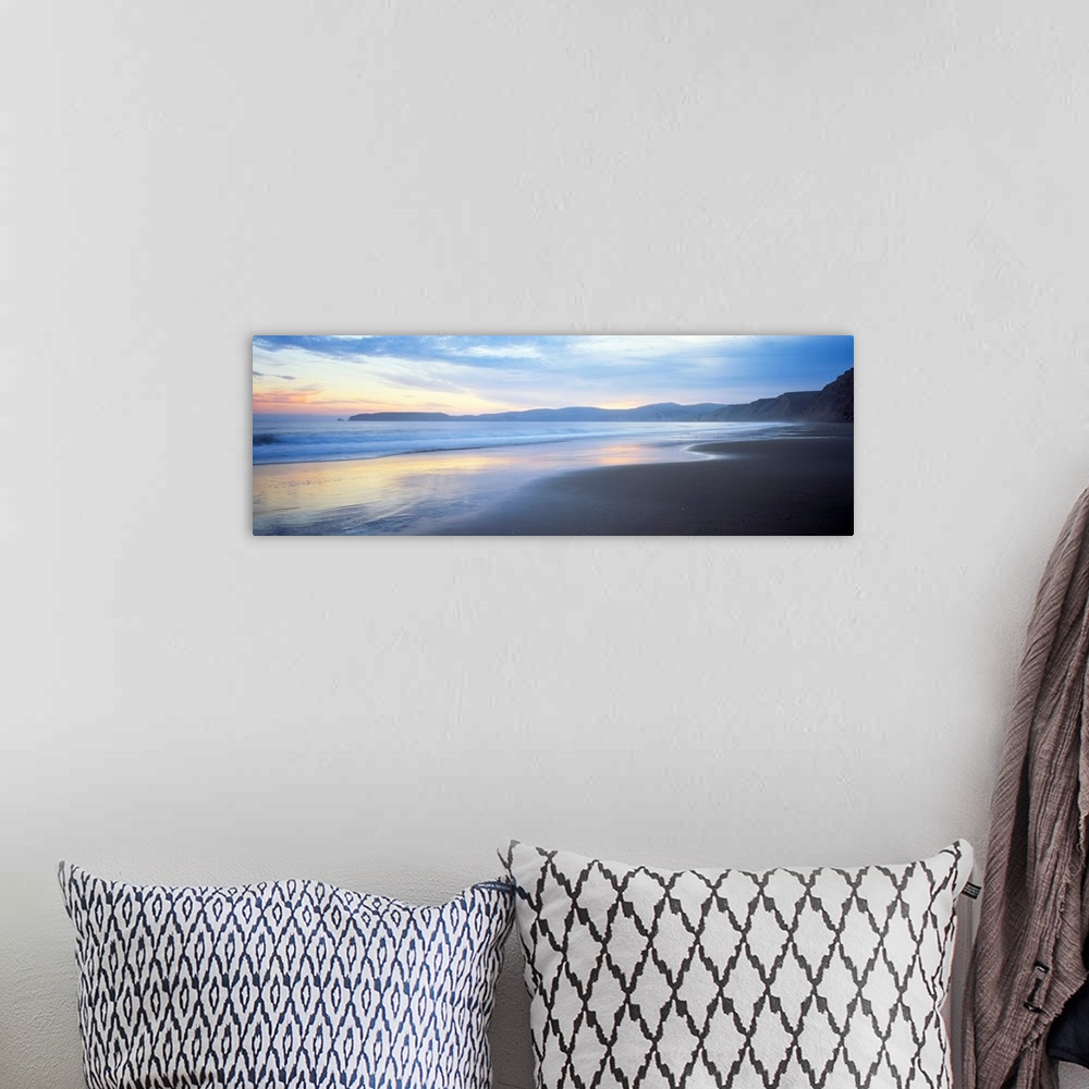 A bohemian room featuring Panoramic photograph shows waves slowly crashing into a section of a beach.  In the background is...