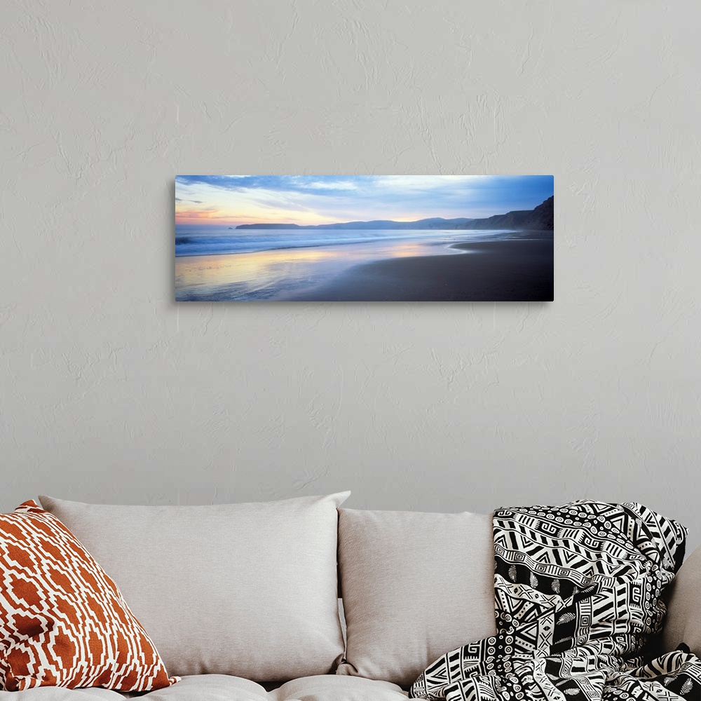 A bohemian room featuring Panoramic photograph shows waves slowly crashing into a section of a beach.  In the background is...