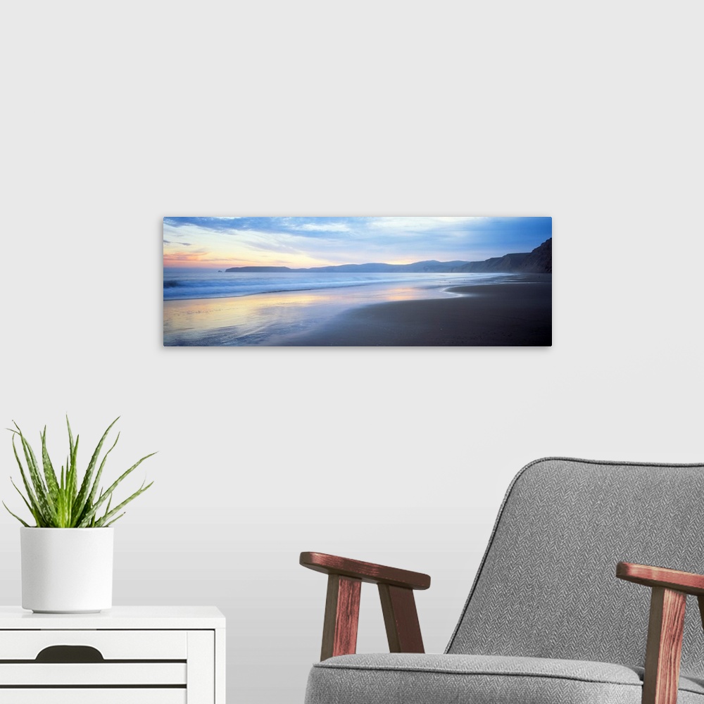 A modern room featuring Panoramic photograph shows waves slowly crashing into a section of a beach.  In the background is...