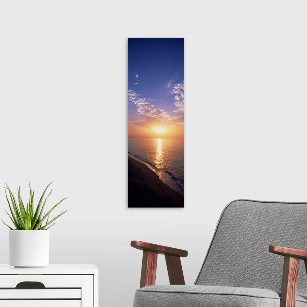 A modern room featuring Vertical panorama of the sun rising on the horizon of the Atlantic ocean, as seen from a sandy be...