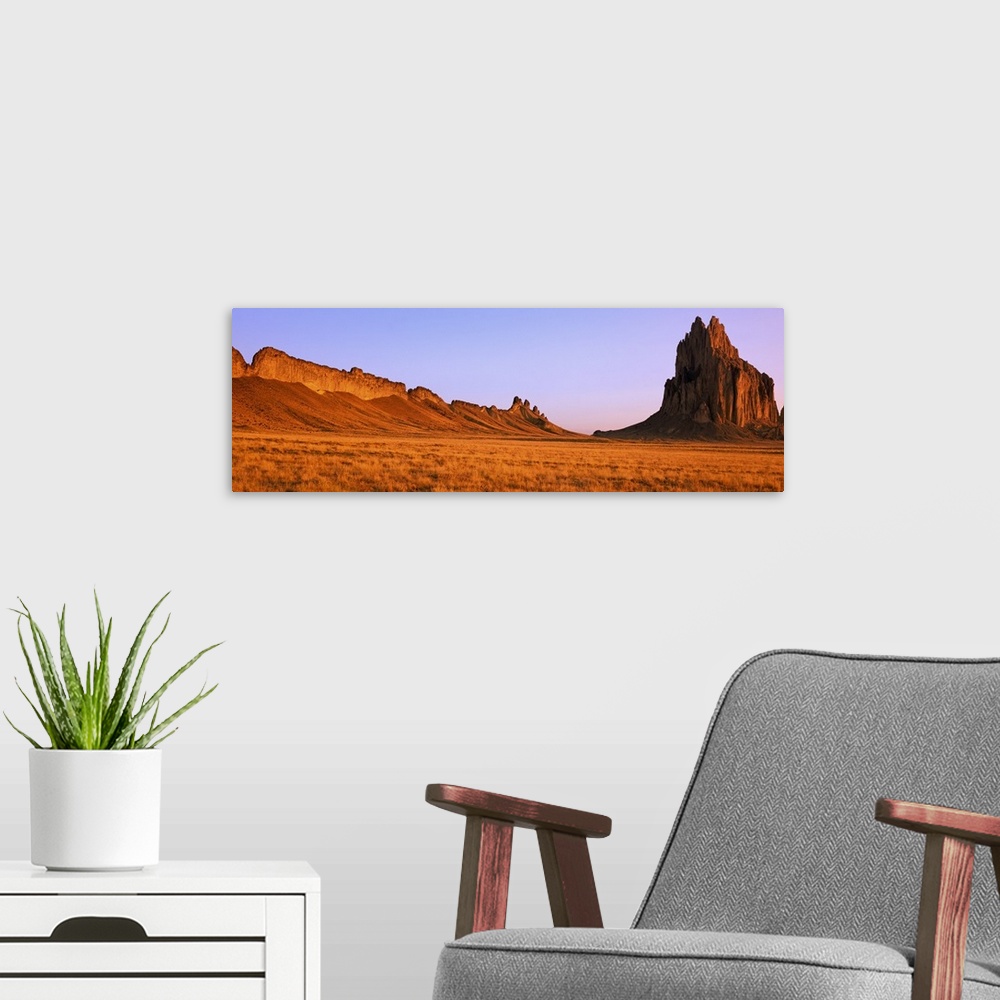 A modern room featuring Ship Rock mountain is skewed to the right side of this panoramic piece with vast desert terrain t...
