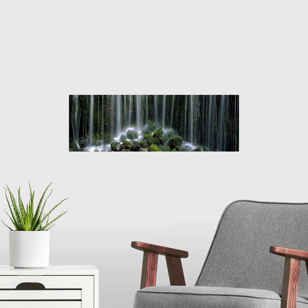 A modern room featuring Panoramic photograph displays a gathering of large rocks covered in moss as the waterfall above c...
