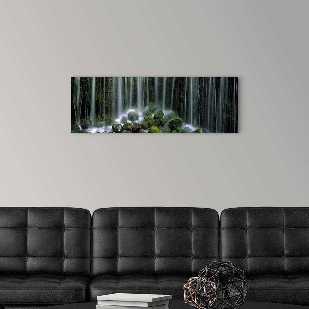 A modern room featuring Panoramic photograph displays a gathering of large rocks covered in moss as the waterfall above c...