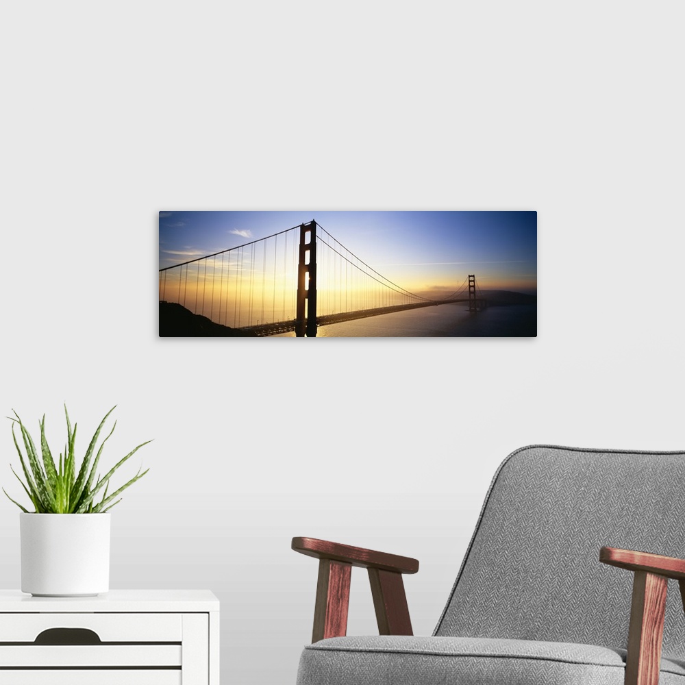 A modern room featuring Panoramic, angled photograph of the Golden Gate Bridge, silhouetted as the sun rises in the sky o...