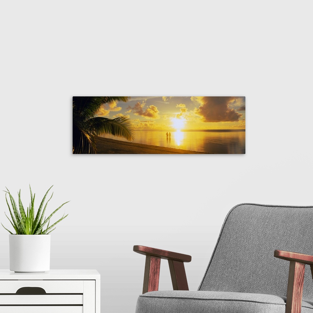 A modern room featuring A panoramic photograph of the sun setting over a tropical sea and cloud filled sky with palm tree...