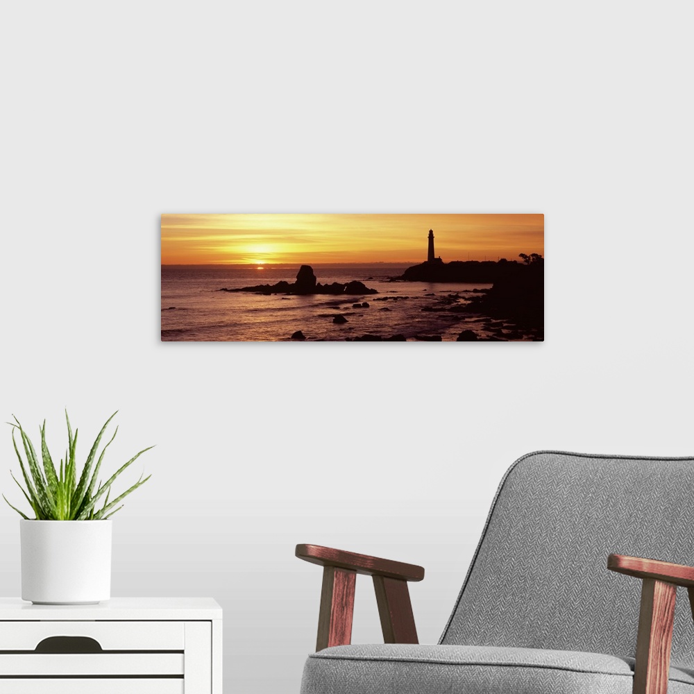 A modern room featuring A lighthouse and the cliffs surrounding it are silhouetted by the sunset over the Pacific ocean.
