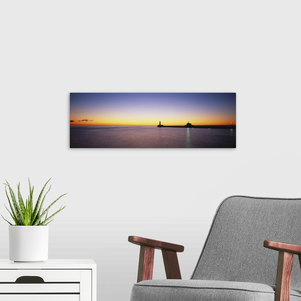 A modern room featuring Panoramic photo on canvas of a lighthouse and pier silhouetted against a sunset.