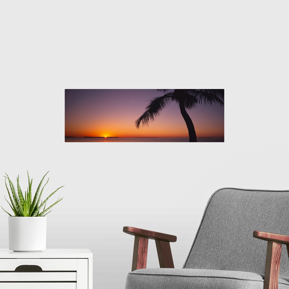 A modern room featuring The last bit of sun is peaking over the horizon illumniating the sky in brilliant oranges and pur...