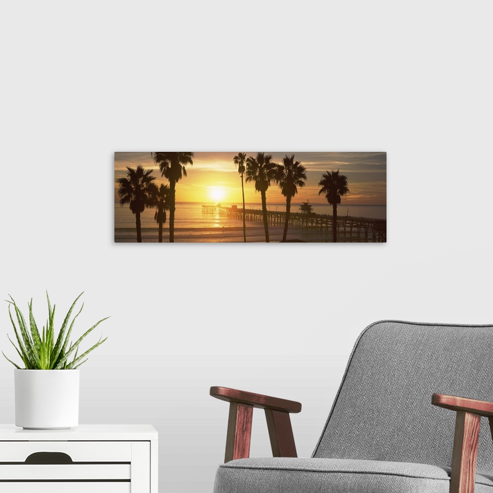 A modern room featuring Panoramic photograph of dock stretching into ocean at sunset with palm tree silhouettes in the fo...