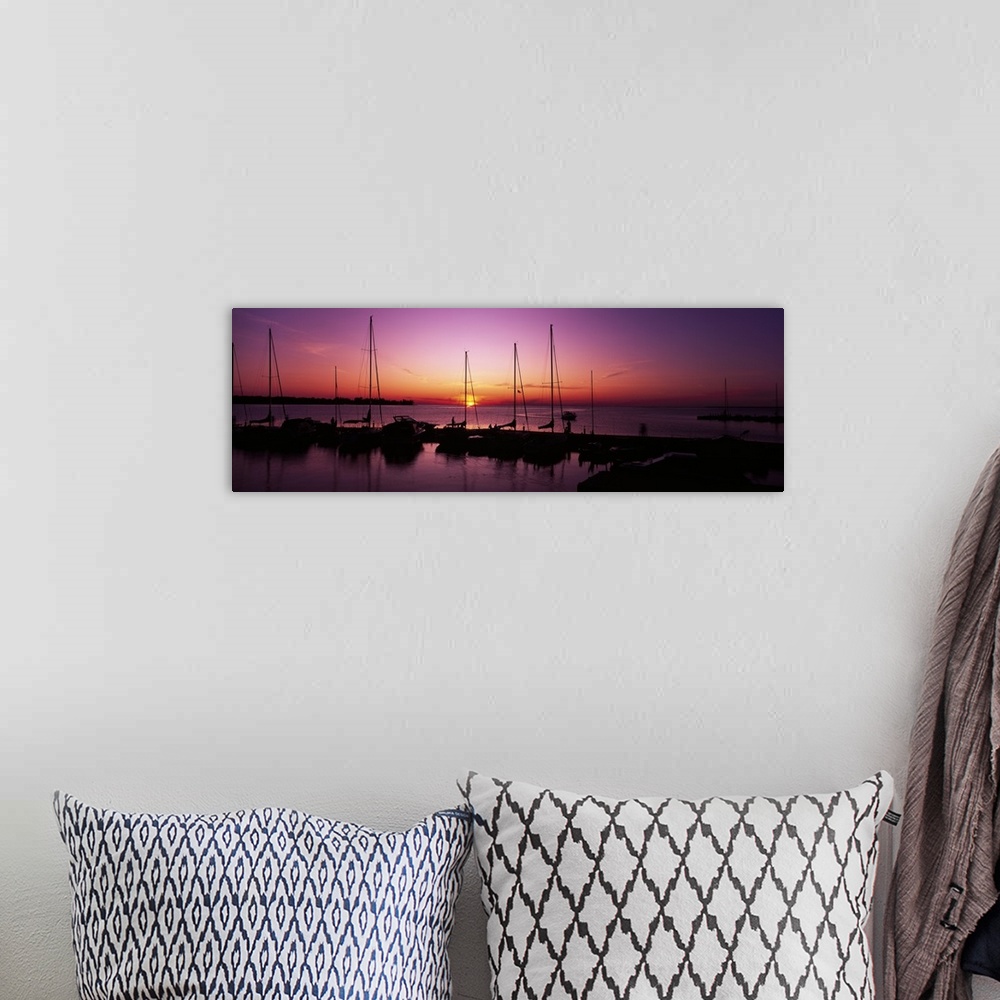 A bohemian room featuring Several boats sit docked and silhouetted by the sunset that is about to dip below the horizon.