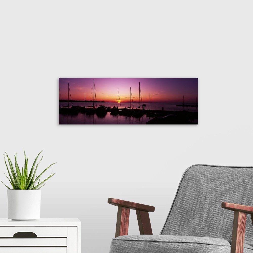 A modern room featuring Several boats sit docked and silhouetted by the sunset that is about to dip below the horizon.