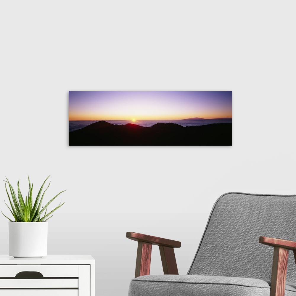 A modern room featuring The sun begins to rise above the horizon and silhouettes a mountain range in the foreground of th...