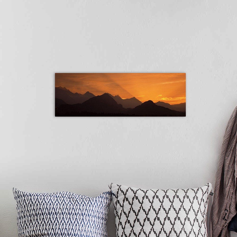 A bohemian room featuring Wide angle photograph of the sun setting behind the silhouetted European Alps, beneath a golden s...