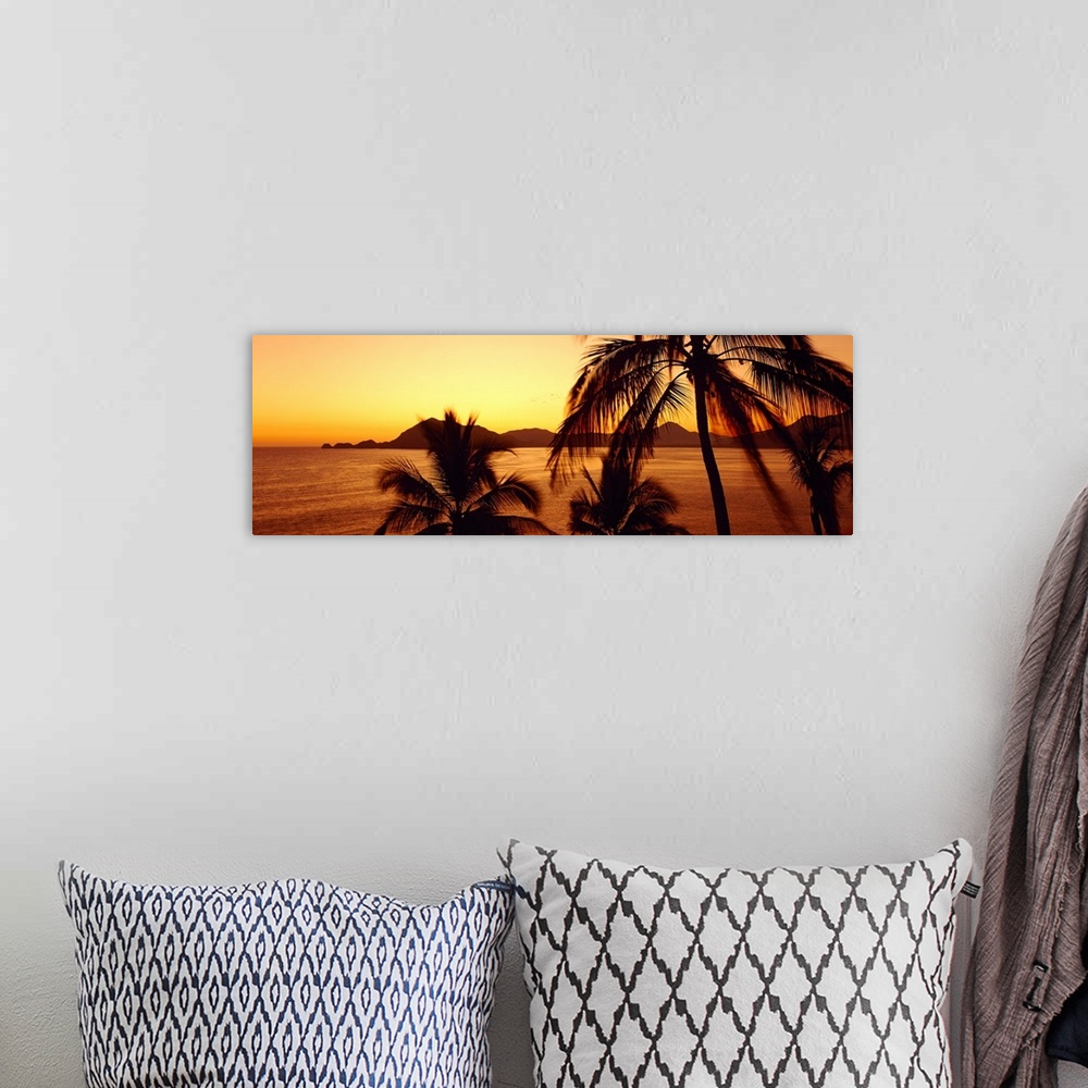 A bohemian room featuring Palm trees stand on the edge of the ocean as the sun sets behind the Mexican hills.
