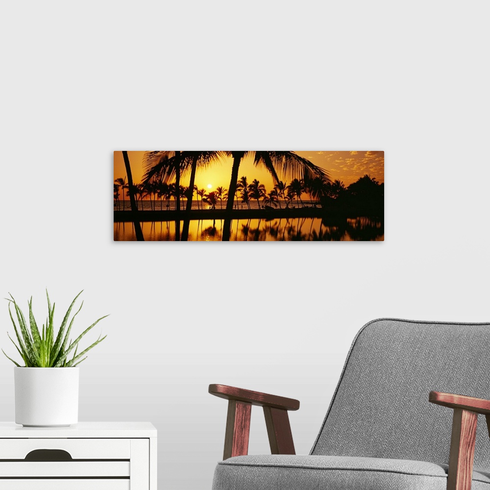 A modern room featuring The sun begins to set over the Pacific ocean and silhouettes a line of palm trees.