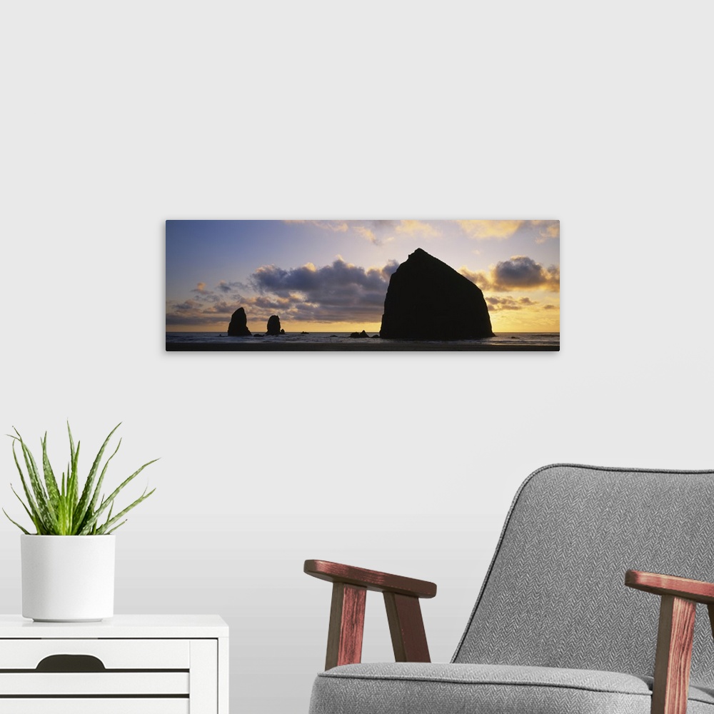 A modern room featuring Large panoramic piece of the sunset that silhouettes rock formations in the ocean.