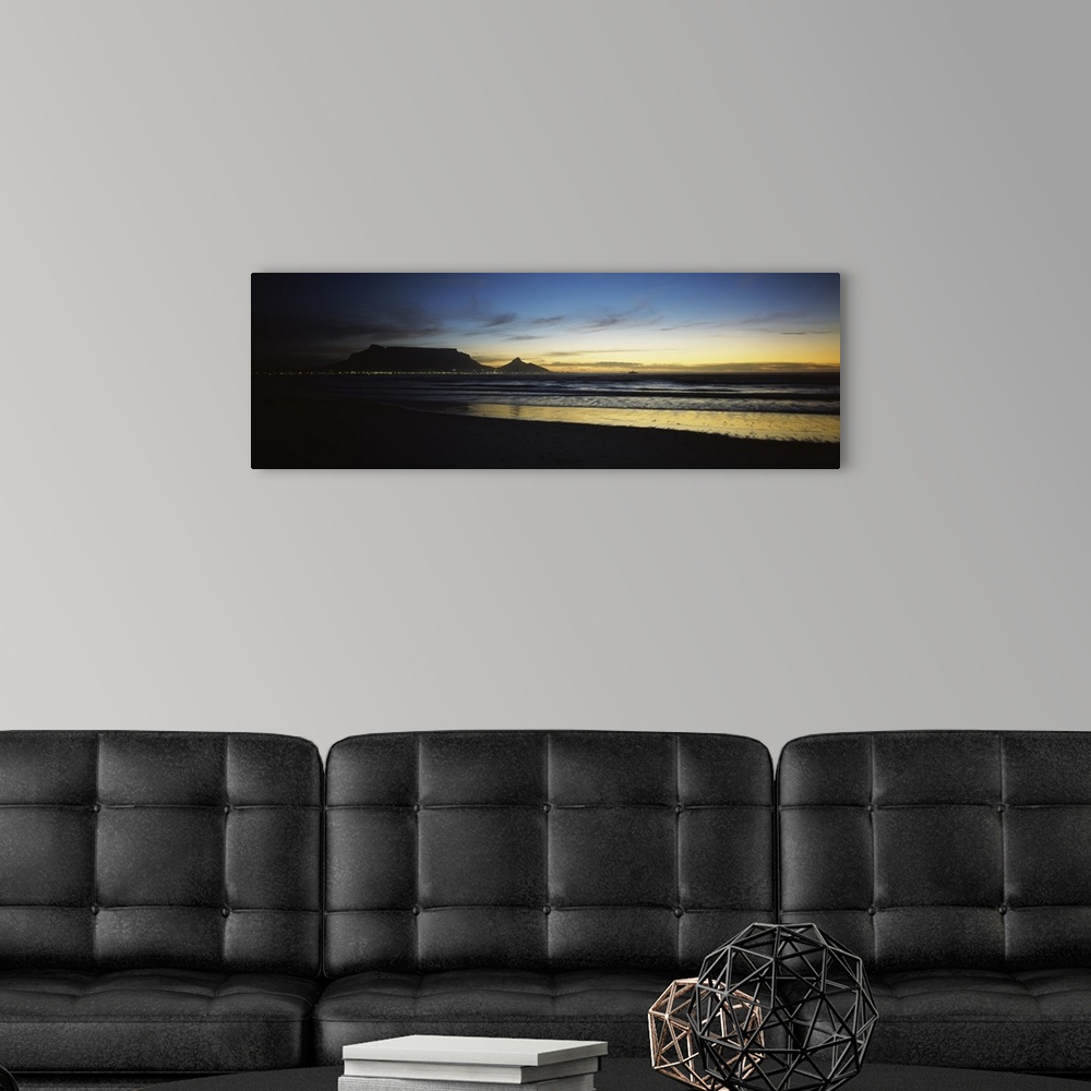 A modern room featuring Panoramic photograph of shoreline at dusk under a cloudy sky with mountain range silhouette in th...