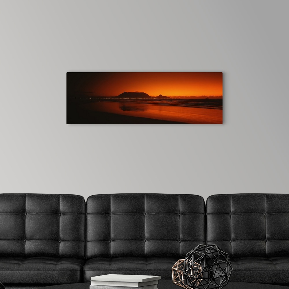 A modern room featuring Wide angle, large photograph of sunset at the shoreline near Table Bay in Western Cape Province, ...