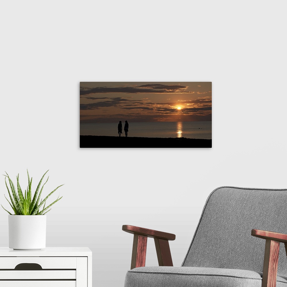 A modern room featuring Panoramic photo of the silhouette of two people walking along the ocean at sunset.