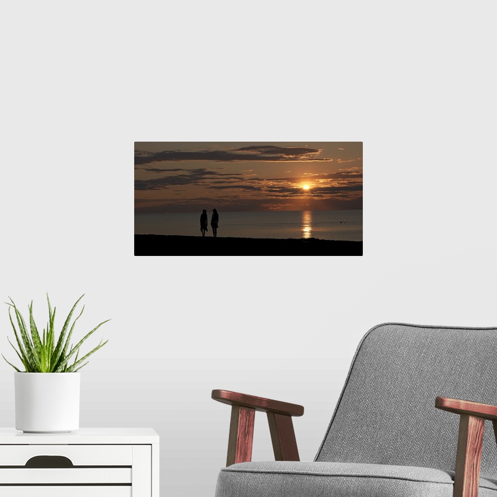 A modern room featuring Panoramic photo of the silhouette of two people walking along the ocean at sunset.
