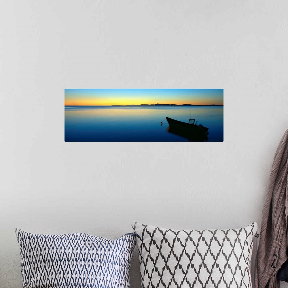 A bohemian room featuring Lonely boat resting on the calm ocean as the fading sun emits a golden glow on the horizon.