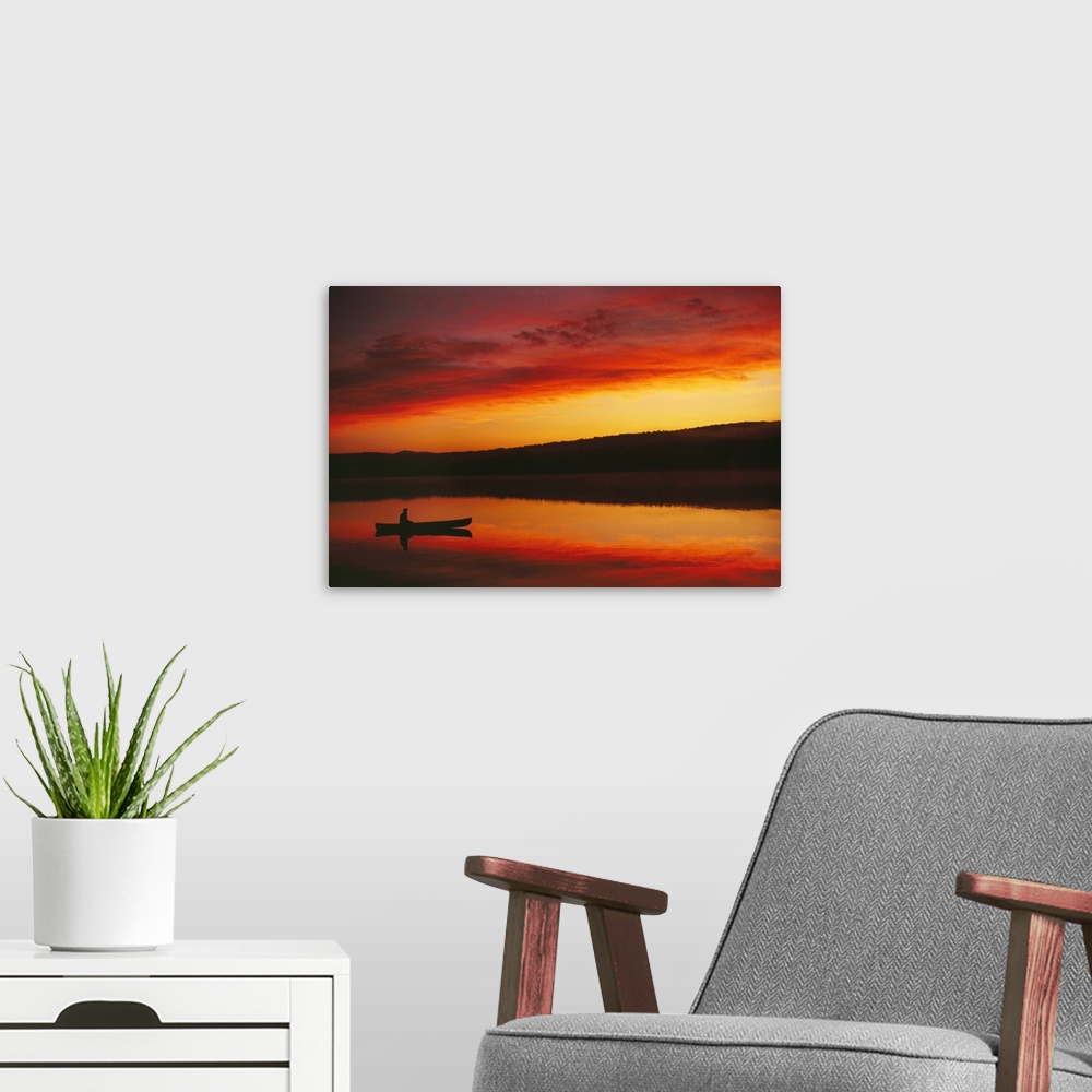 A modern room featuring Big, landscape photograph of the silhouette of a person sitting in a boat beneath a vibrant, fier...