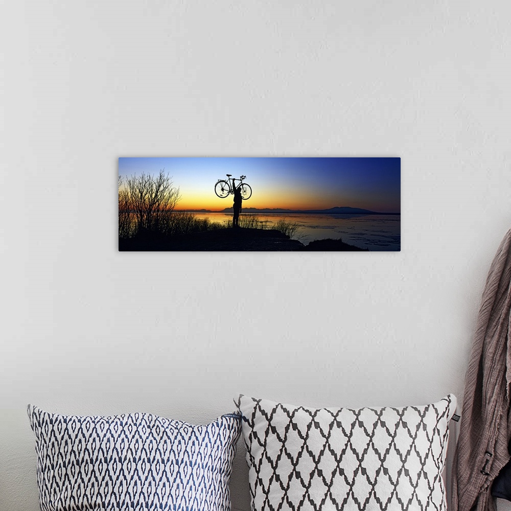A bohemian room featuring Panoramic photograph of man holding bike in air at shoreline at dusk with mountains in the distance.