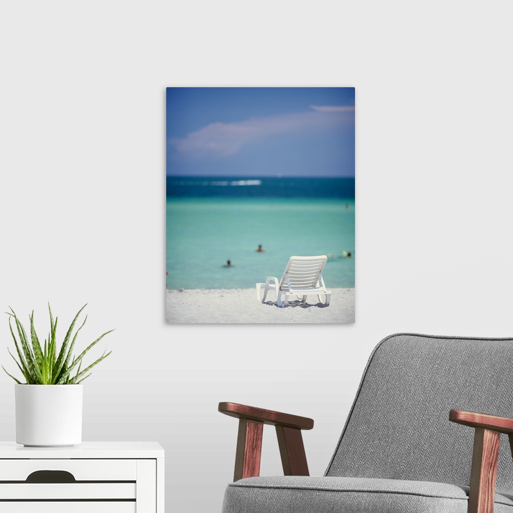 A modern room featuring This vertical piece is of a single lounge chair sitting on the white sand with the ocean and sky ...