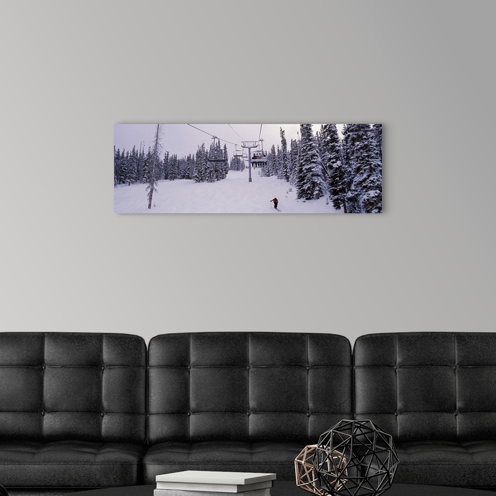 A modern room featuring Panoramic photograph on a giant canvas of a ski lift surrounded by snow covered trees, one skier ...