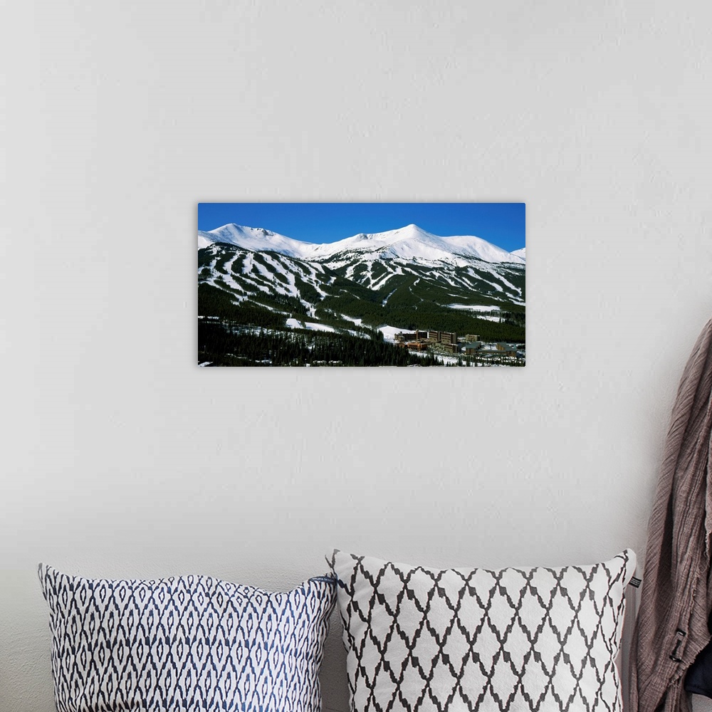 A bohemian room featuring Ski lodges are shown at the bottom of snowy, forested mountain range in this large photograph.