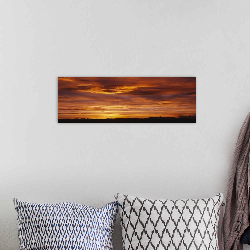 A bohemian room featuring Long panoramic image of the sun setting on the horizon creating a brilliant color show of fire-li...